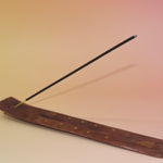 The Buddha Wooden Incense Burner with an incense stick on a pink and yellow background.