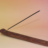 The Buddha Wooden Incense Burner with an incense stick on a pink and yellow background.