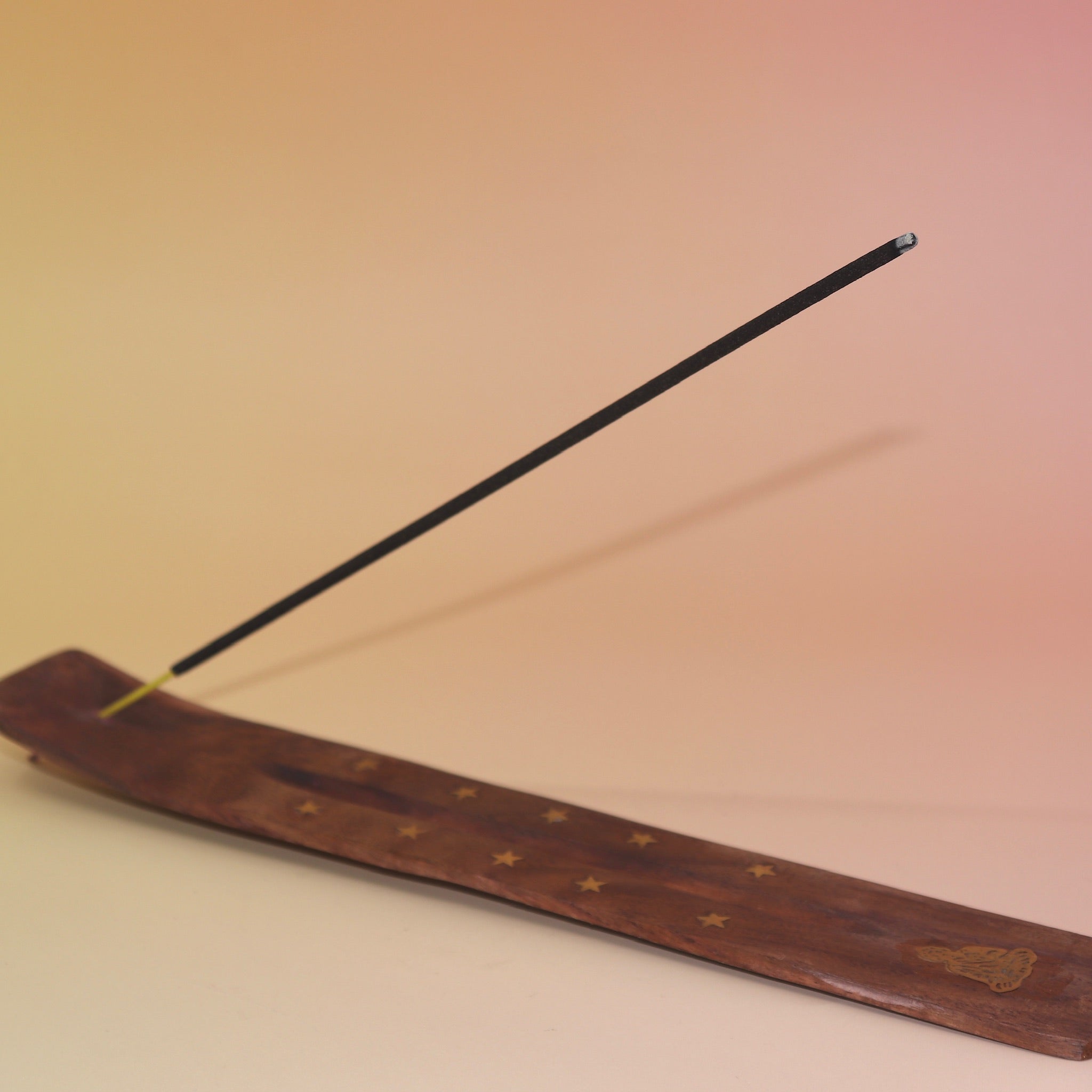 The Buddha Wooden Incense Burner with an incense stick on a pink and yellow background.