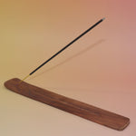 The Plain Wooden Incense Burner with an incense stick on a pink and yellow background.