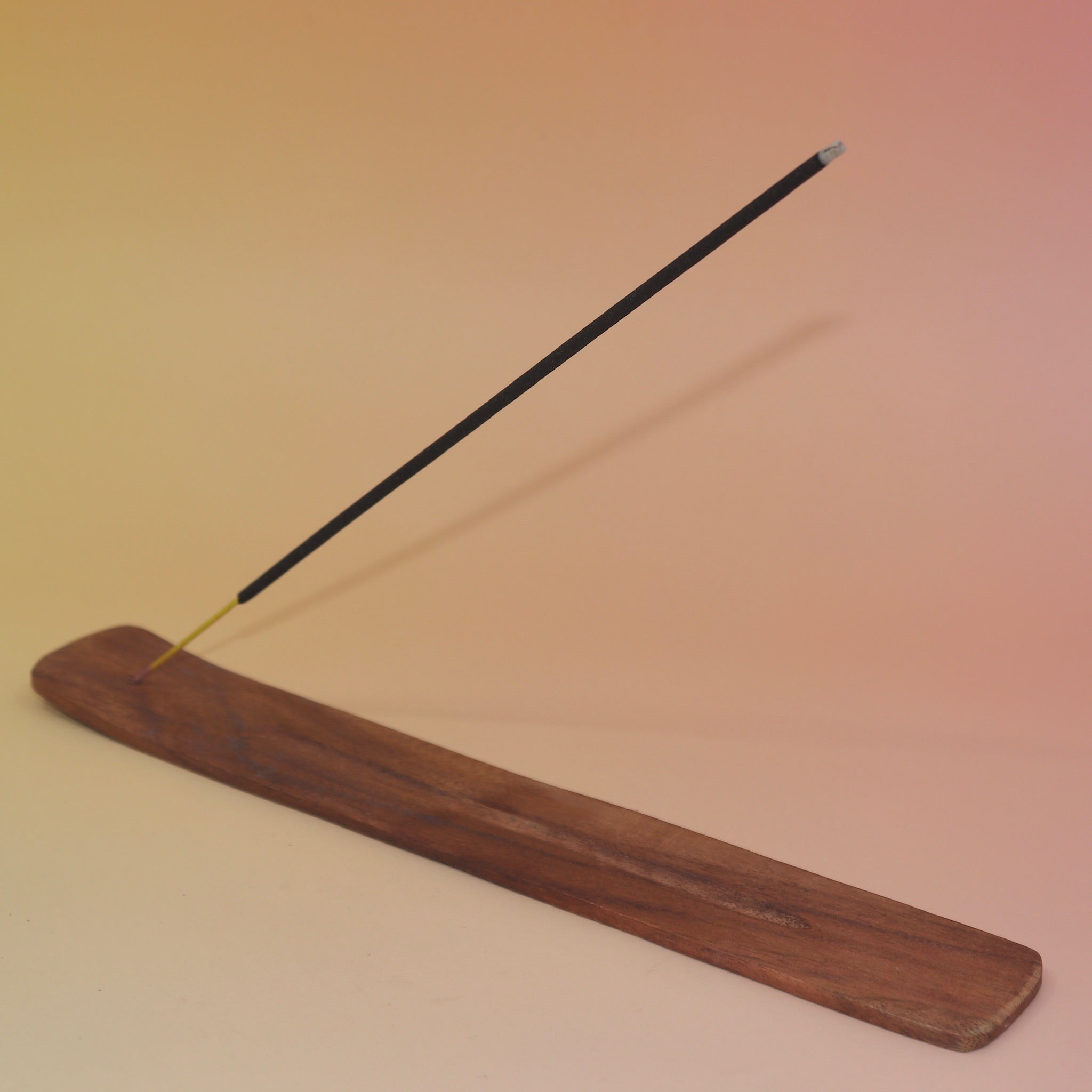 The Plain Wooden Incense Burner with an incense stick on a pink and yellow background.