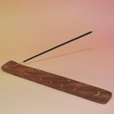 The Moon Wooden Incense Burner with an incense stick on a pink and yellow background.