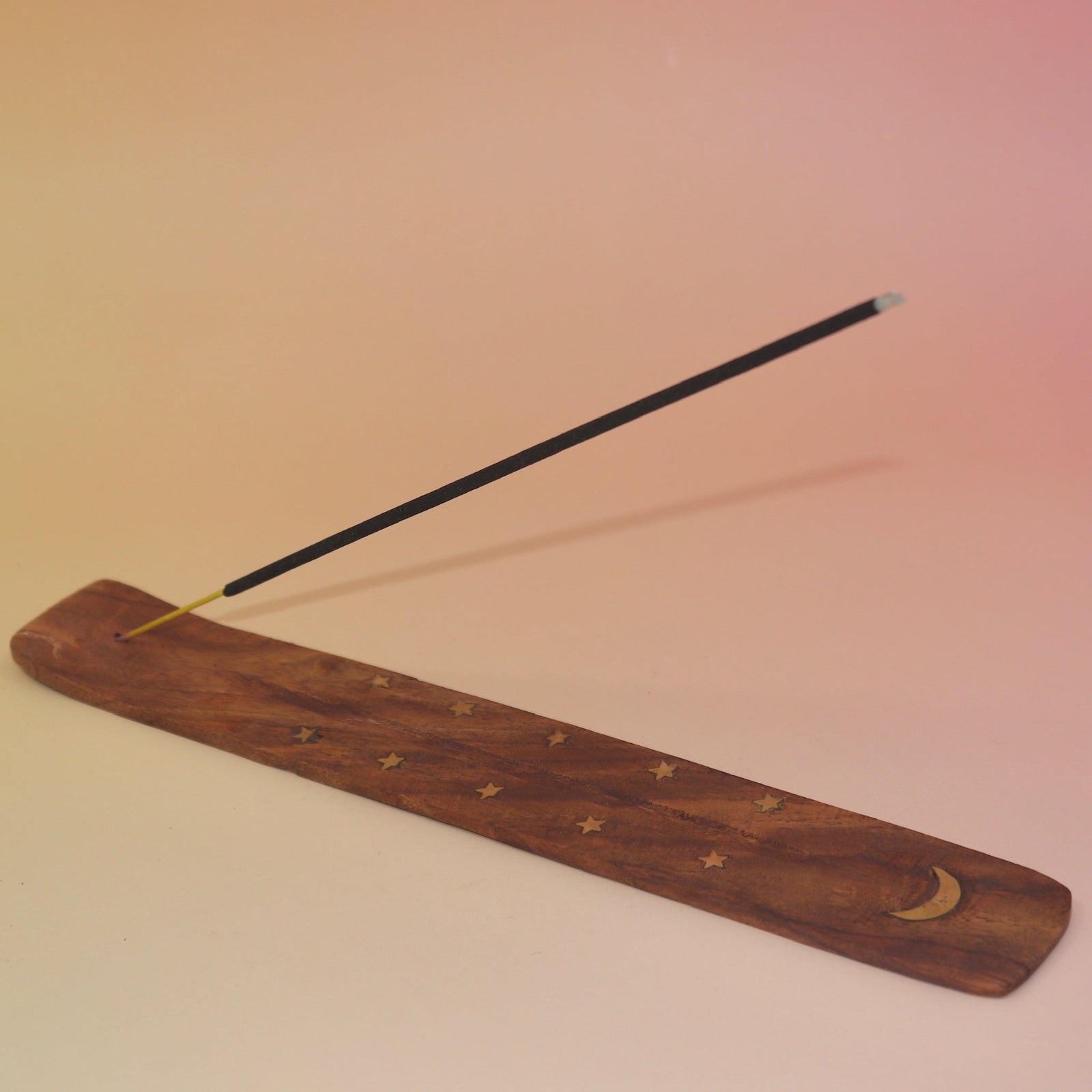 The Moon Wooden Incense Burner with an incense stick on a pink and yellow background.
