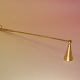 The Brass Candle Snuffer on a pink and yellow background.