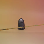The Brass Candle Snuffer on a pink and yellow background in front on a small is crystal tower. 