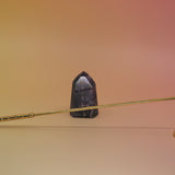 The Brass Candle Snuffer on a pink and yellow background in front on a small is crystal tower. 