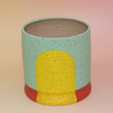 The Betty Multicolored Portal Stoneware 5 in. Planter on a pink and yellow background.