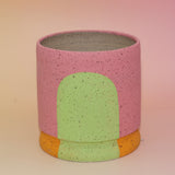 The Stacey Multicolored Portal Stoneware 5 in. Planter on a pink and yellow background.