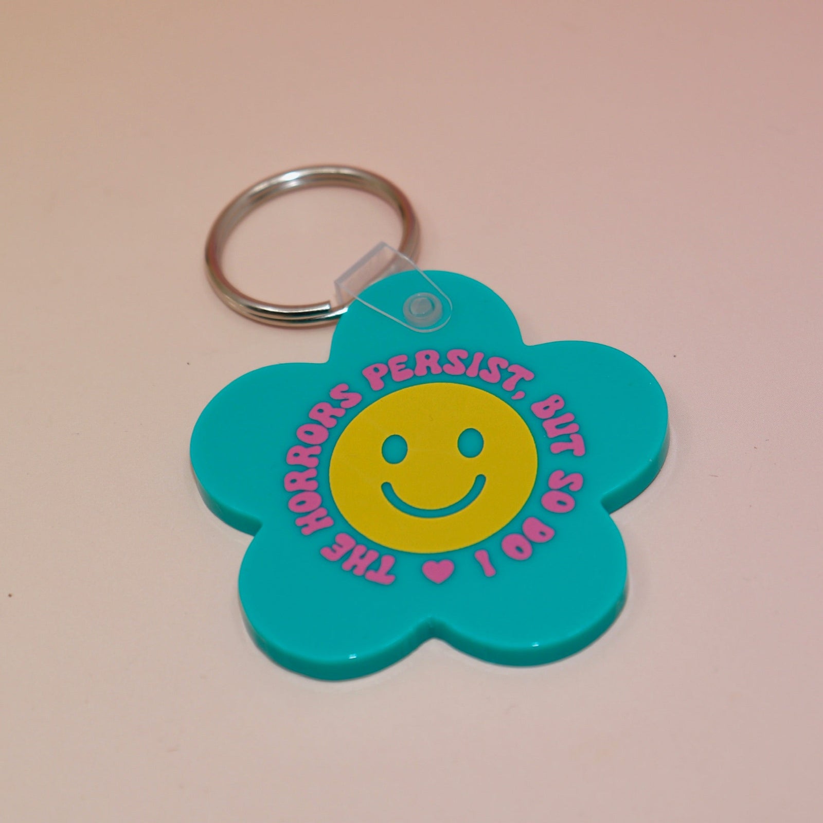 The Horrors Persist But So Do I Flower Shaped Vinyl Keychain on a light pink background.