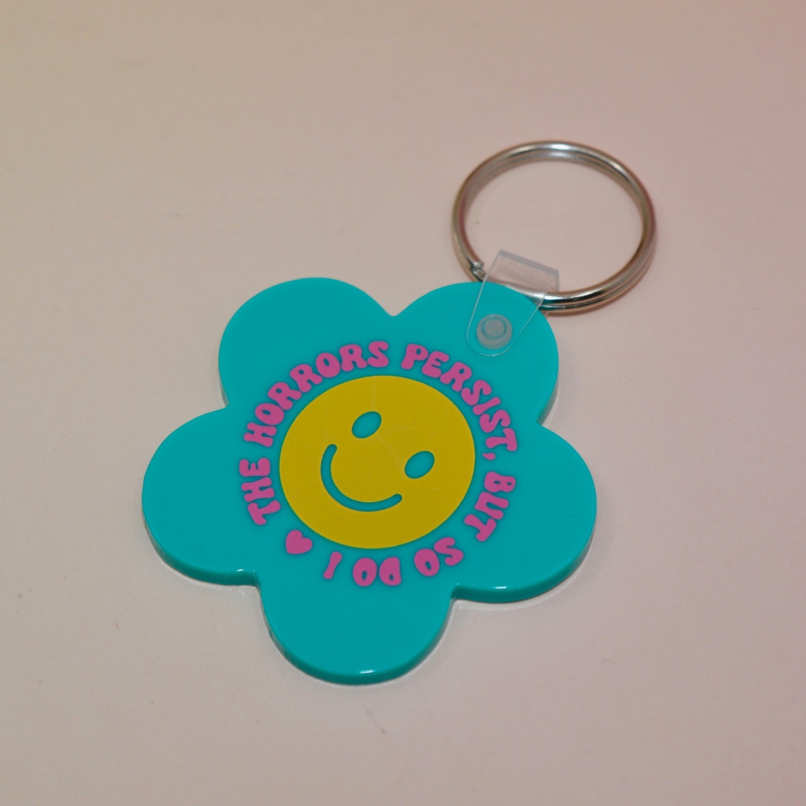 The Horrors Persist But So Do I Flower Shaped Vinyl Keychain on a light pink background.
