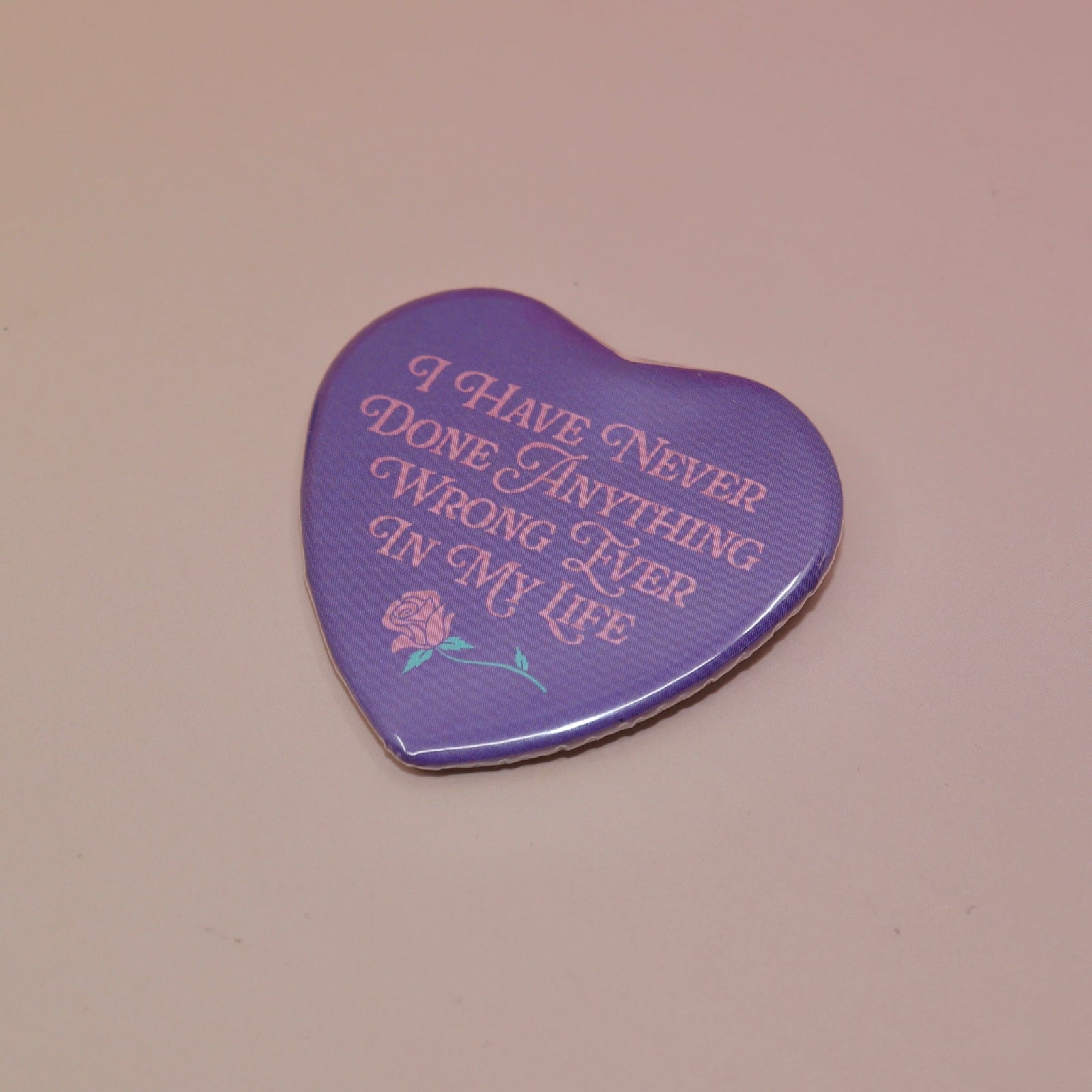 The I Have Never Done Anything Wrong Heart Shaped Pinback Button on a light pink background.