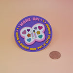 The Wake Up Grab A Brush Makeup SOAD Holographic Glitter Vinyl Sticker next to a quarter on a light pink background.