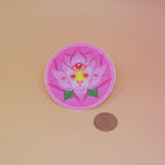 The Four Eared Lotus 3” Round Vinyl Sticker next to a quarter on a light pink background.