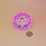 The Four Eared Lotus 3” Round Vinyl Sticker next to a quarter on a light pink background.