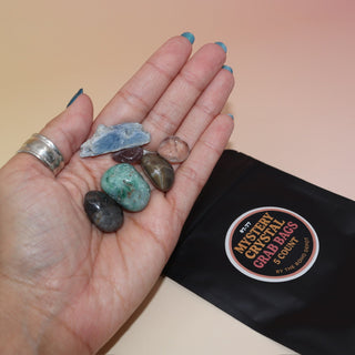 The Mystery Crystal Grab Bag - 5 Count on a pink and yellow background with its contents out of the bag.
