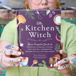 A woman holding the The Kitchen Witch Hardcover Book.