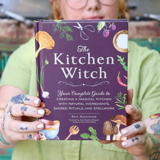 A woman holding the The Kitchen Witch Hardcover Book.