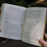 A woman holding open the The Kitchen Witch Hardcover Book to show off its pages.