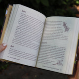 A woman holding open the The Kitchen Witch Hardcover Book to show off its pages.