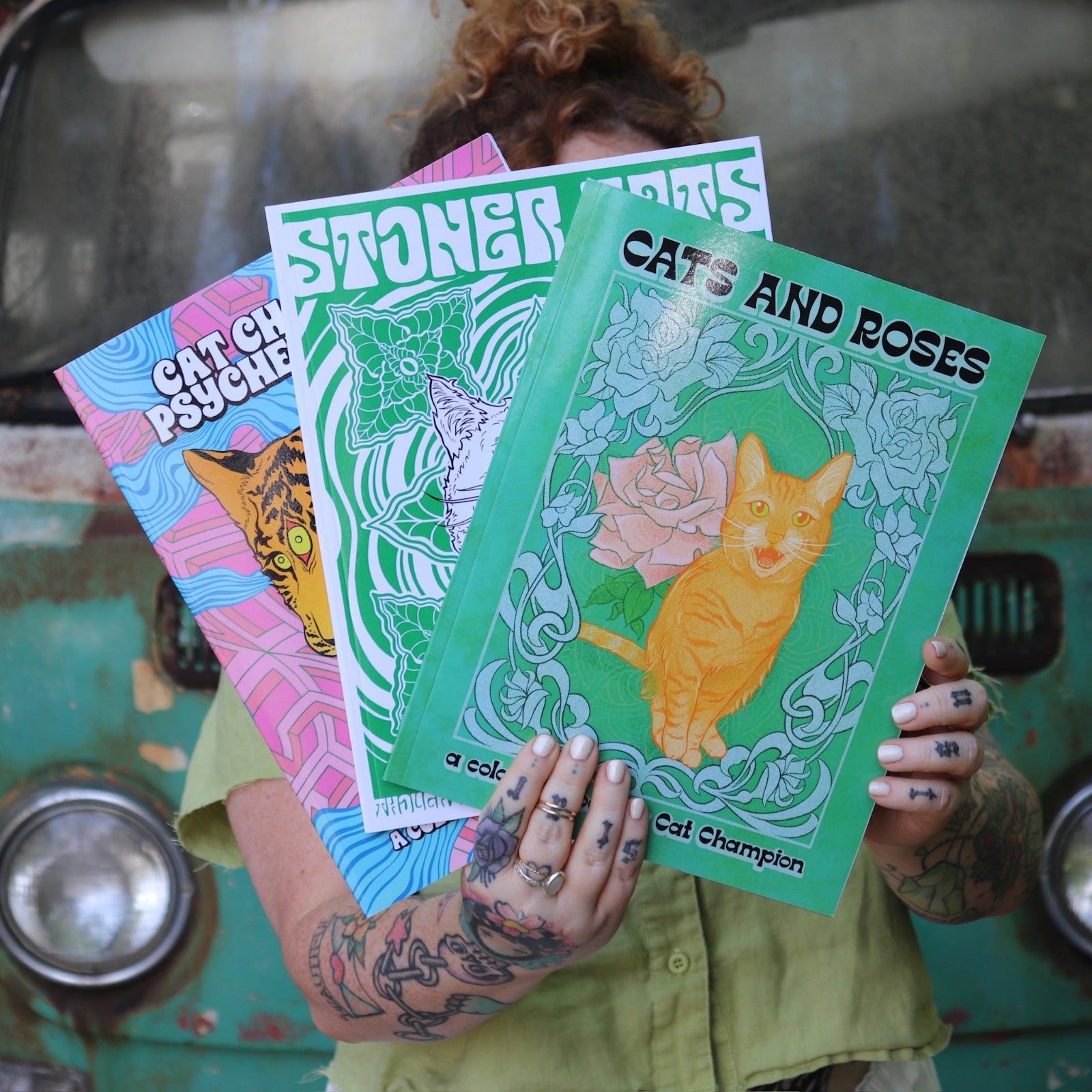 A woman holding all three of the Cat Champion cat coloring books.