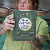 A woman holding the Feral Self-Care Hardcover Book.