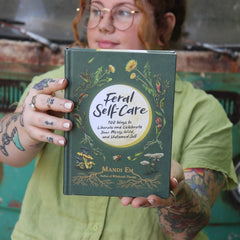A woman holding the Feral Self-Care Hardcover Book.