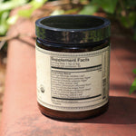 The back of the Liver Vitality Greens - 4oz Powder Daily Cleanser on a red surface with greenery to its right.