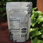 The back of the Heirloom Cacao - Ancestral Cacao Powder on a rusty red surface next to ivy.