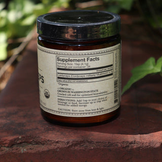 The side of the Cordyceps Energy Super Tonic Mushroom Powder on a red surface next to greenery.
