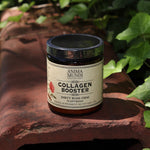The Collagen Booster - Dirty Rose Chai 4oz Powder on a rusty red surface surrounded by green ivy.