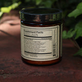 The back of the Golden Moon Milk - 5oz Blue Lotus Vanilla Powder on a red surface next to ivy.