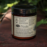 The side of the Golden Moon Milk - 5oz Blue Lotus Vanilla Powder on a red surface next to ivy.
