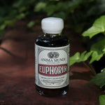 The Euphoria Elixir - 4oz Aphrodisiac Tonic on a red surface next to greenery.