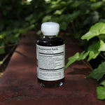 The back of the Euphoria Elixir - 4oz Aphrodisiac Tonic on a red surface next to greenery.