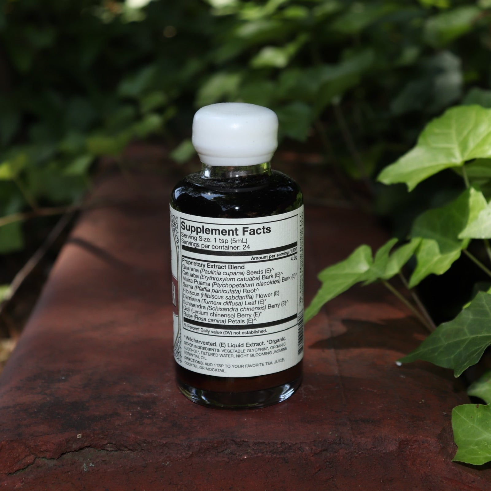 The back of the Euphoria Elixir - 4oz Aphrodisiac Tonic on a red surface next to greenery.