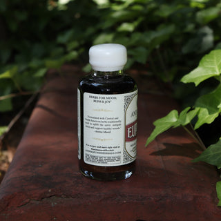 The side of the Euphoria Elixir - 4oz Aphrodisiac Tonic on a red surface next to greenery.