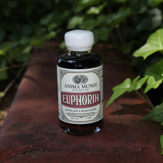 The Euphoria Elixir - 4oz Aphrodisiac Tonic on a red surface next to greenery.