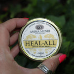 Someone holding the Heal-All Arnica - Nourish, Soothe + Repair Relief Balm in front of ivy.