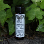 The Tulsi - Holy Basil Essential Oil on a concrete surface in front of a patch of ivy.