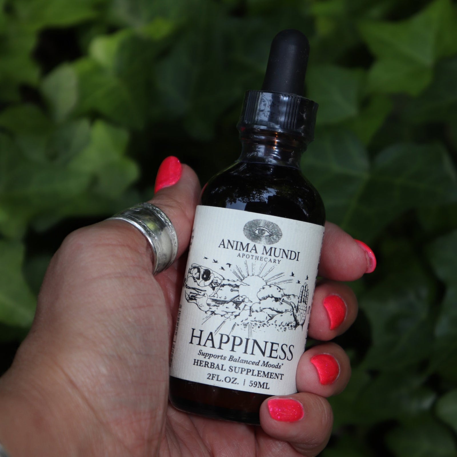 Someone holding the Happiness Tonic - 2 fl. oz. Adaptogenic Spirit Tonic in front of a patch of ivy.