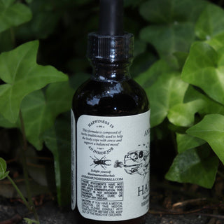 The Happiness Tonic - 2 fl. oz. Adaptogenic Spirit Tonic on a graphite surface in front of a patch of ivy.