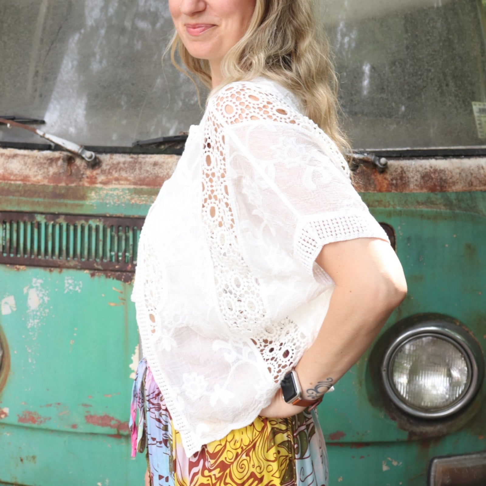 A woman wearing the white Lace Open Front Cardigan with Batwing Sleeves with tie-dye bottoms and crochet top.