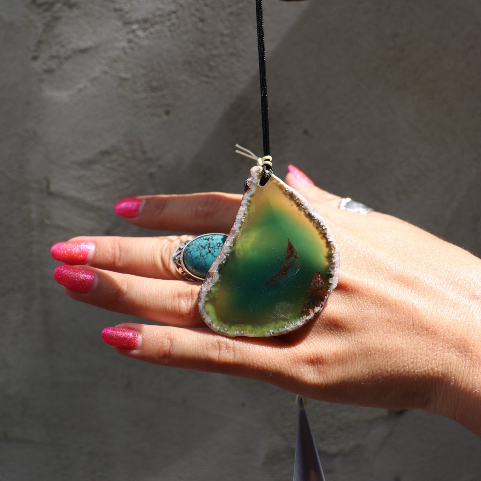 Someone holding the agate slice from the Woodstock Agate Celtic Chime in front of a concrete wall.