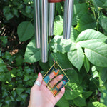 Someone holding the Vienna Art Deco Woodstock Wind Chime in front of a bush. 