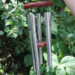 Someone holding the Vienna Art Deco Woodstock Wind Chime in front of a bush. 