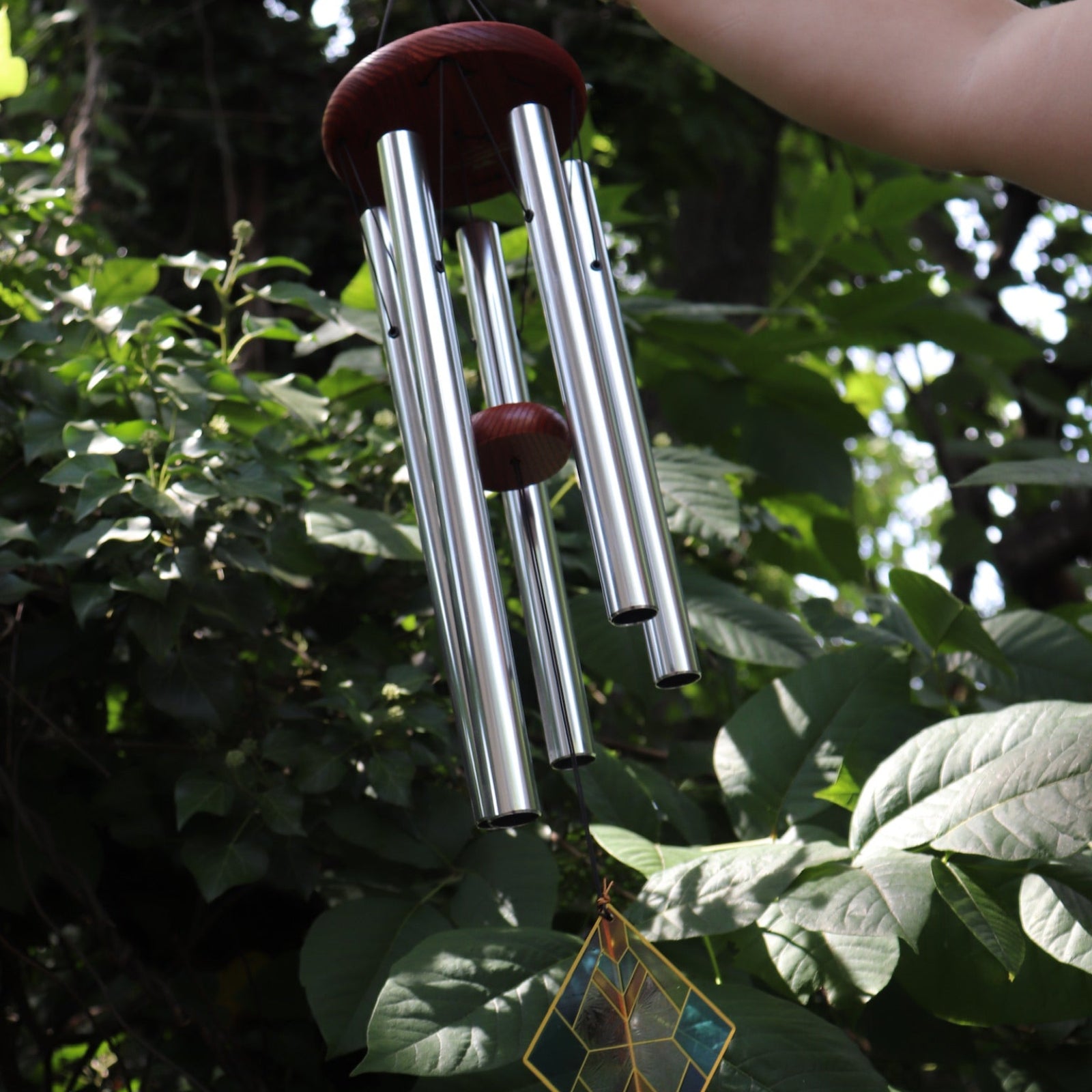 Someone holding the Vienna Art Deco Woodstock Wind Chime in front of a bush. 
