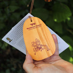 Someone holding the wooden clapper from the Tibetan Prayer Wind Chime in front of a bush.