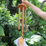 Someone holding the Tibetan Prayer Wind Chime in front of a bush.