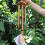 Someone holding the Tibetan Prayer Wind Chime in front of a bush.