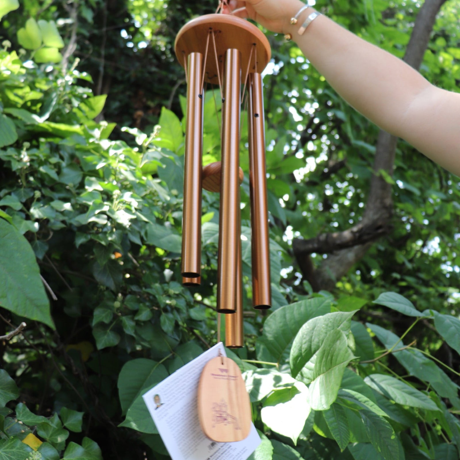 Someone holding the Tibetan Prayer Wind Chime in front of a bush.